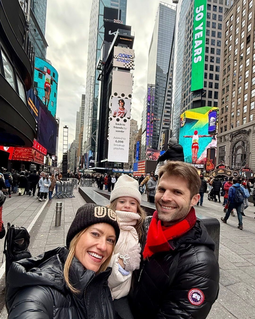 14 Places to Travel With Family: Beaches, Parks and Cities 1 Family of three smiling for a selfie in bustling Times Square, New York City.
