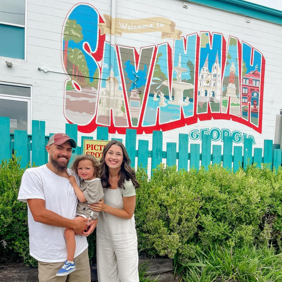 14 Places to Travel With Family: Beaches, Parks and Cities 9 Family posing in front of a colorful Savannah Georgia welcome mural and blue fence