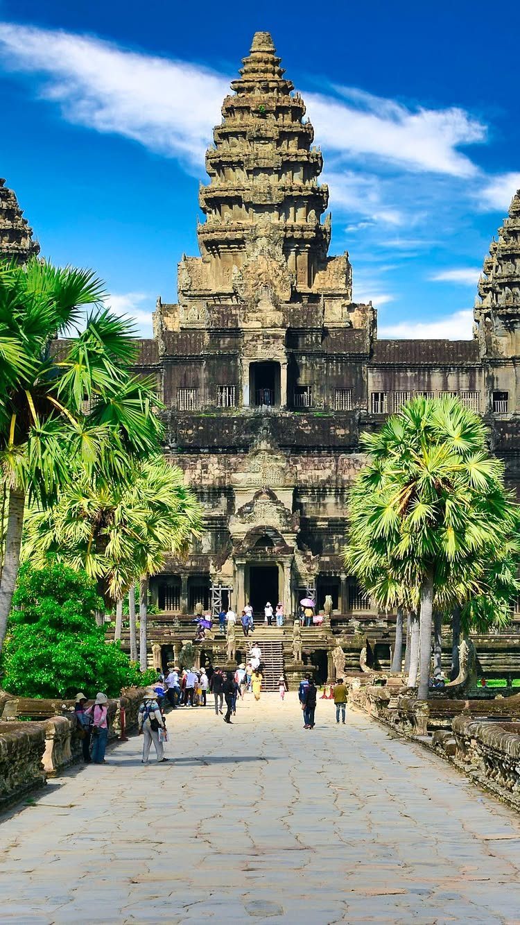 Places to Visit Around the World: 23 Ideas With Photos 12 Angkor Wat temple complex with stone towers, palm trees, and tourists on a walkway.