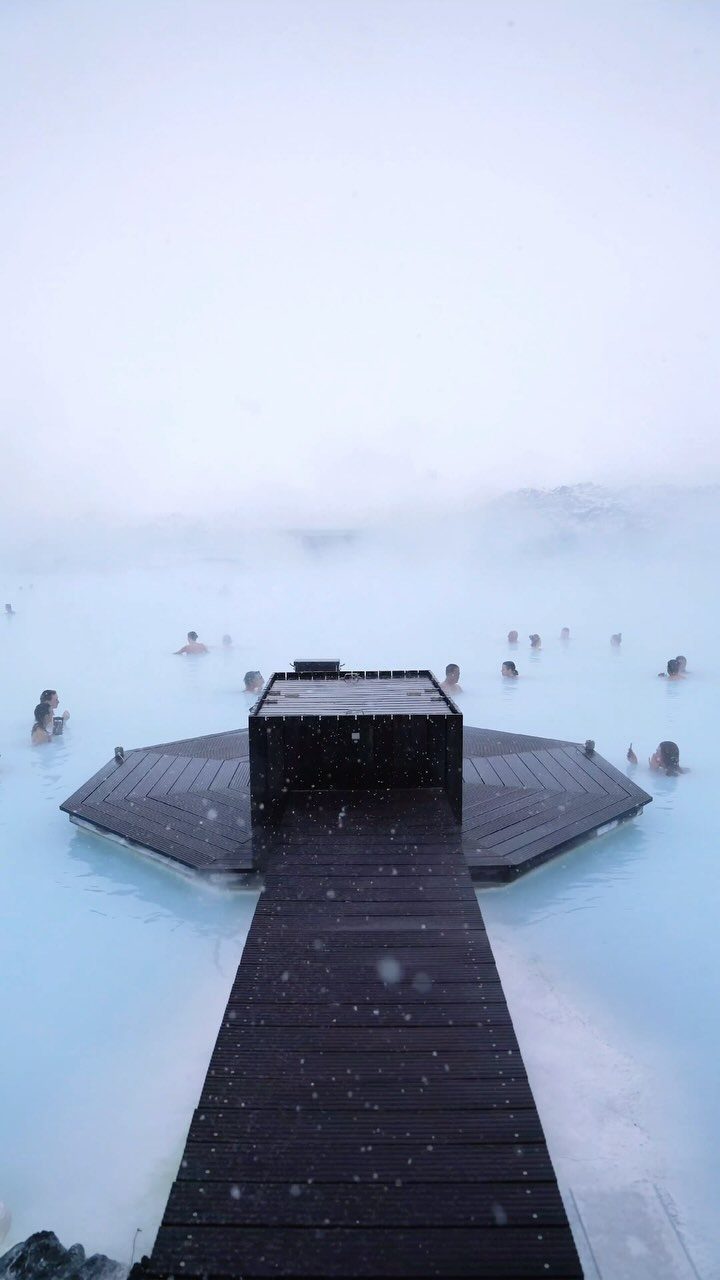 Places to Visit Around the World: 23 Ideas With Photos 8 Wooden boardwalk leading into milky blue geothermal waters with people bathing in steam