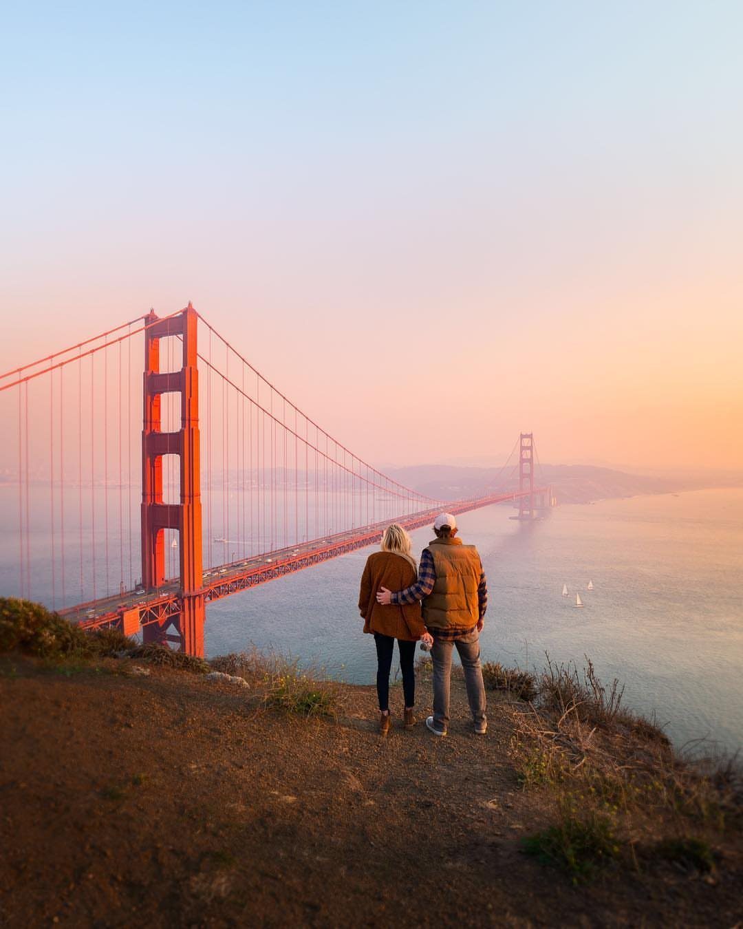 Places to Visit Around the World: 23 Ideas With Photos 19 Couple standing on a cliff overlooking the Golden Gate Bridge at sunset