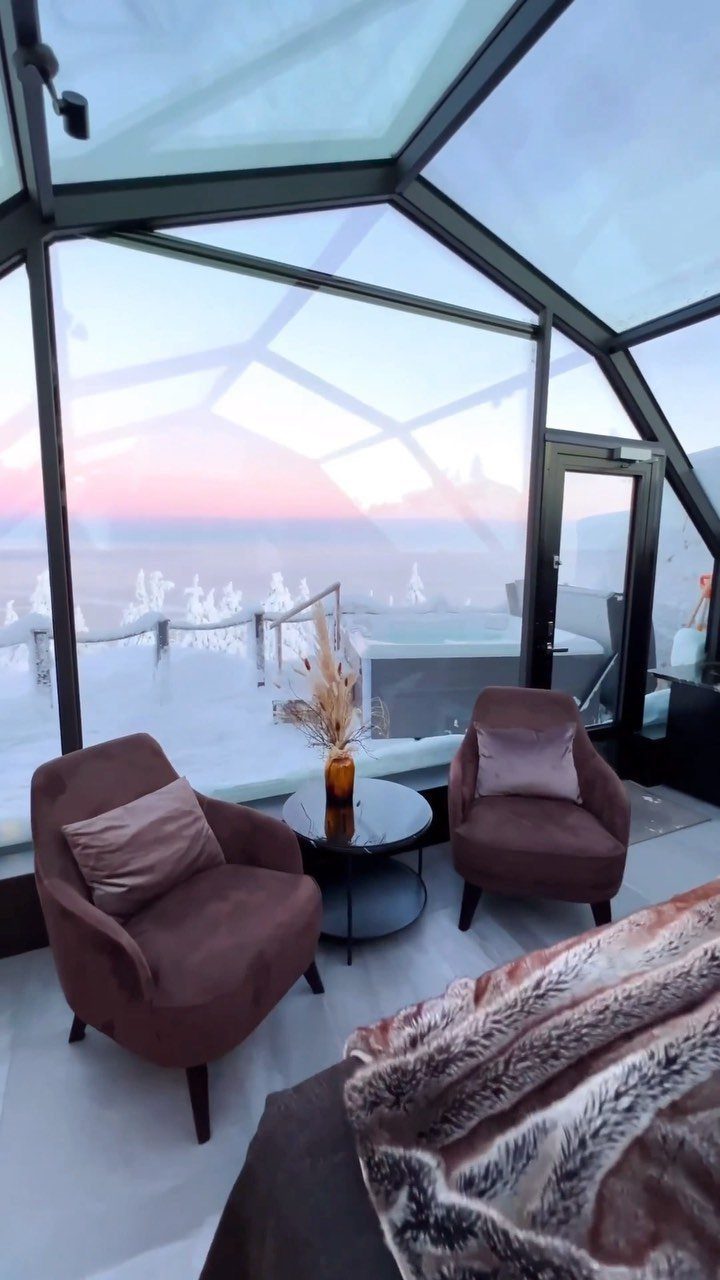Places to Visit Around the World: 23 Ideas With Photos 20 Glass igloo interior with brown chairs overlooking a snowy landscape at twilight.