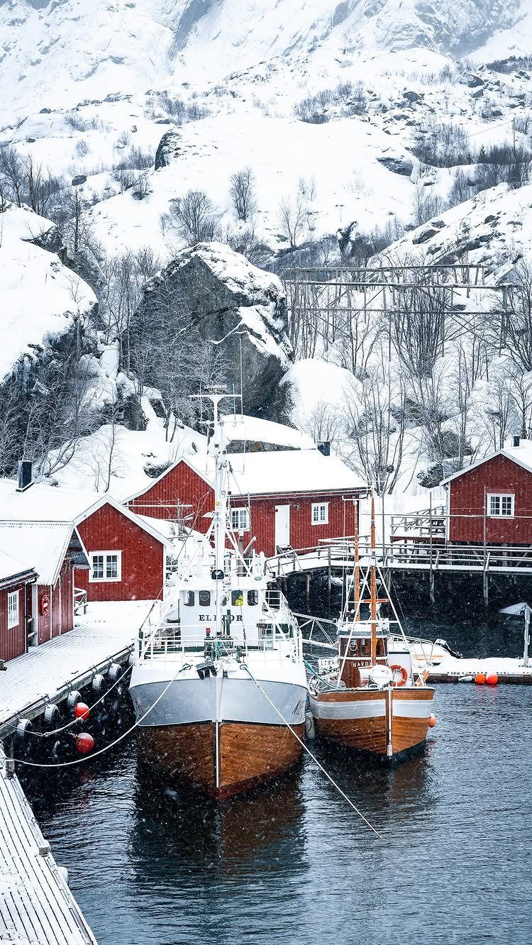 Places to Visit Around the World: 23 Ideas With Photos 14 Fishing boats docked by red cabins with snow-covered mountains in the background.