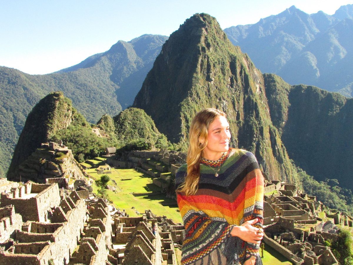 Places to Visit Around the World: 23 Ideas With Photos 6 Woman in colorful poncho posing before the stone ruins of Machu Picchu, Peru.