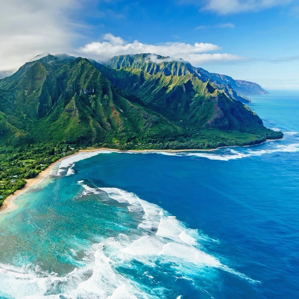 Places to Visit Around the World: 23 Ideas With Photos 21 Lush green mountains meeting a turquoise ocean with white crashing waves on shore.