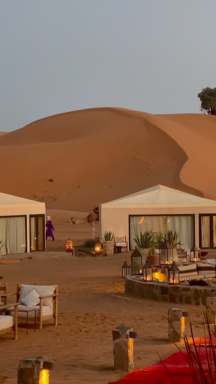 Places to Visit Around the World: 23 Ideas With Photos 15 Luxury desert camp with white tents and lanterns before large orange sand dunes