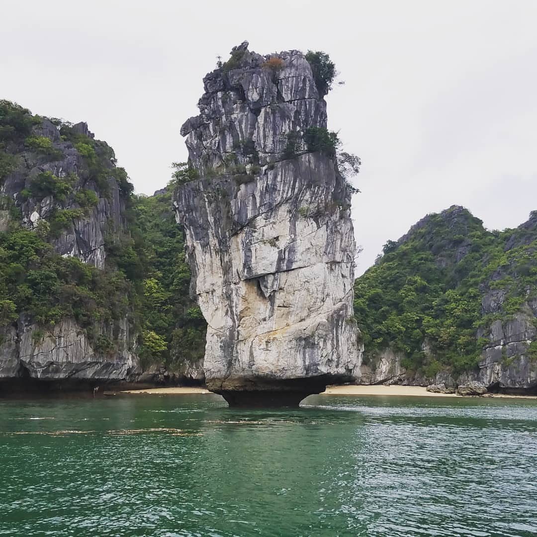 Prettiest Place to Visit: 21 Ideas Around the World 6 Tall limestone karst pillar rising from emerald green water in Halong Bay.