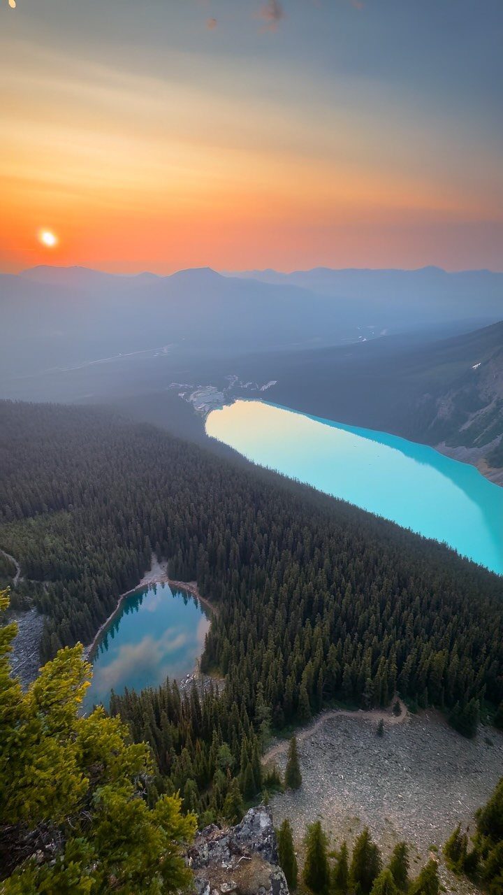 Prettiest Place to Visit: 21 Ideas Around the World 13 Turquoise lake surrounded by pine forests and mountains under a glowing orange sunset.