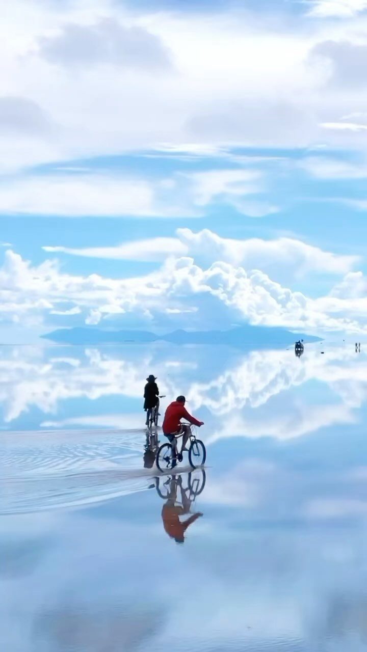 Prettiest Place to Visit: 21 Ideas Around the World 12 Two cyclists riding across the reflective white surface of Salar de Uyuni salt flats.