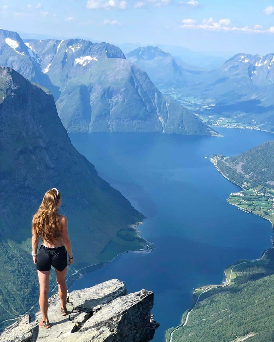 13 Pretty Countries to Visit for Coasts, Peaks and Ruins 4 Woman standing on a rocky cliff overlooking a deep blue Norwegian fjord and mountains