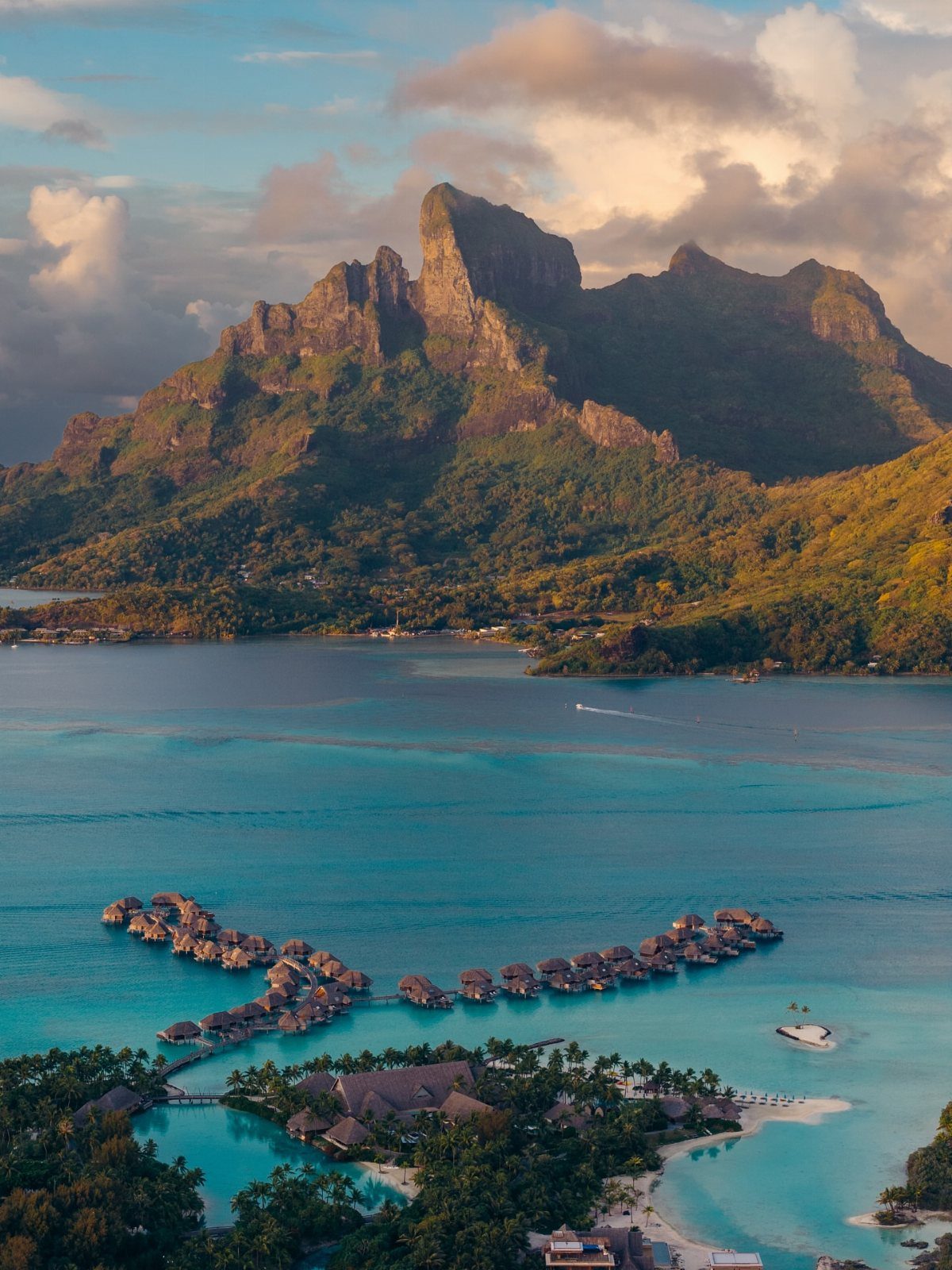 26 Pretty Places Around the World, From Fjords to Falls 5 Overwater bungalows in turquoise water with a large green mountain in the background.