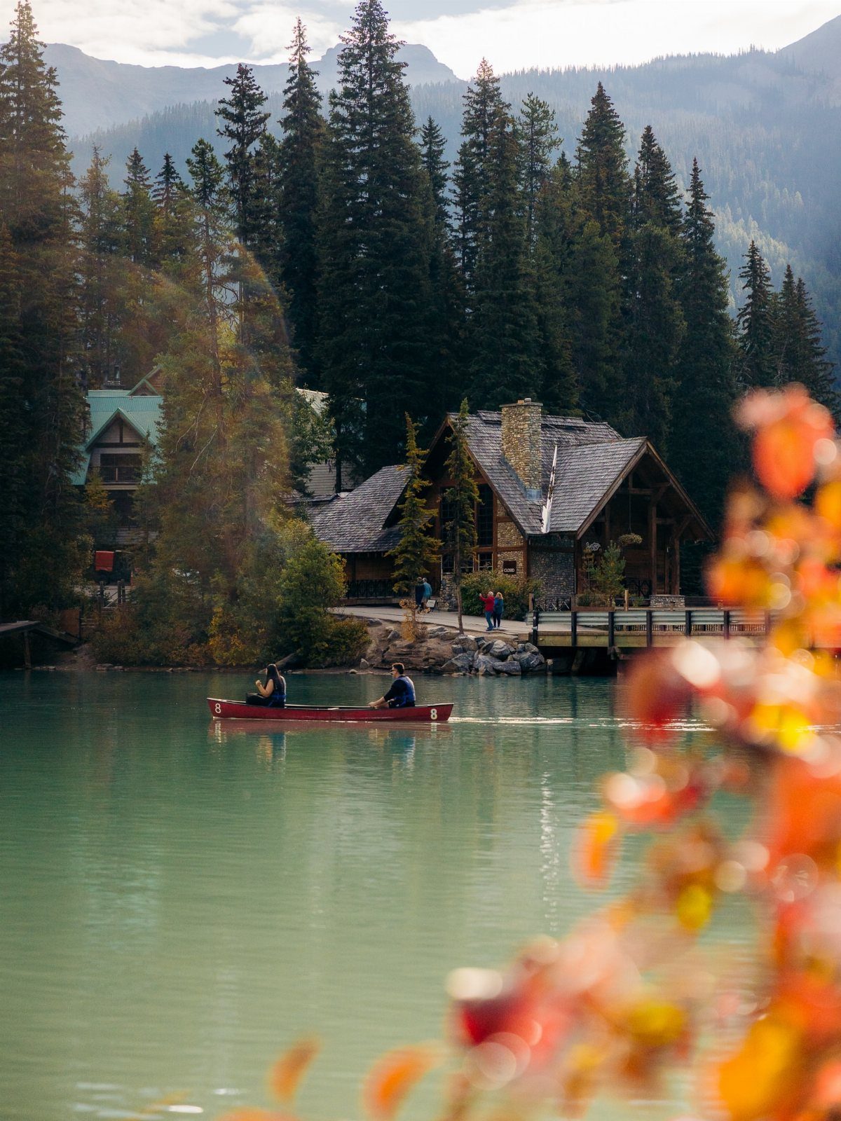 26 Pretty Places Around the World, From Fjords to Falls 24 Two people canoeing on a turquoise lake near a rustic wooden lodge and mountains.