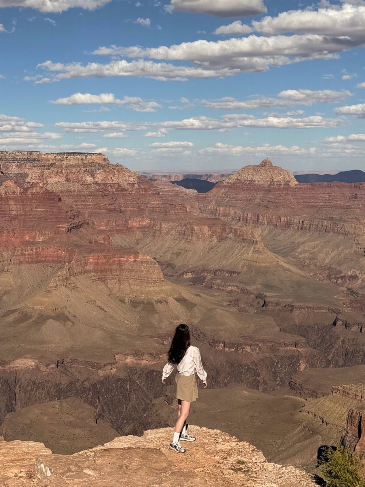 26 Pretty Places Around the World, From Fjords to Falls 4 Woman standing on a cliff overlooking the expansive red rock Grand Canyon landscape.