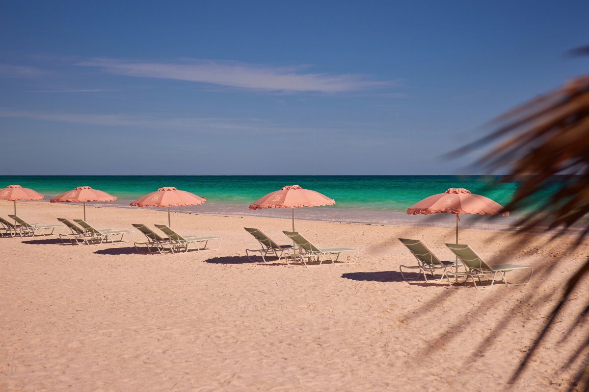 26 Pretty Places Around the World, From Fjords to Falls 21 Pink sand beach with pink umbrellas and lounge chairs under a blue sky