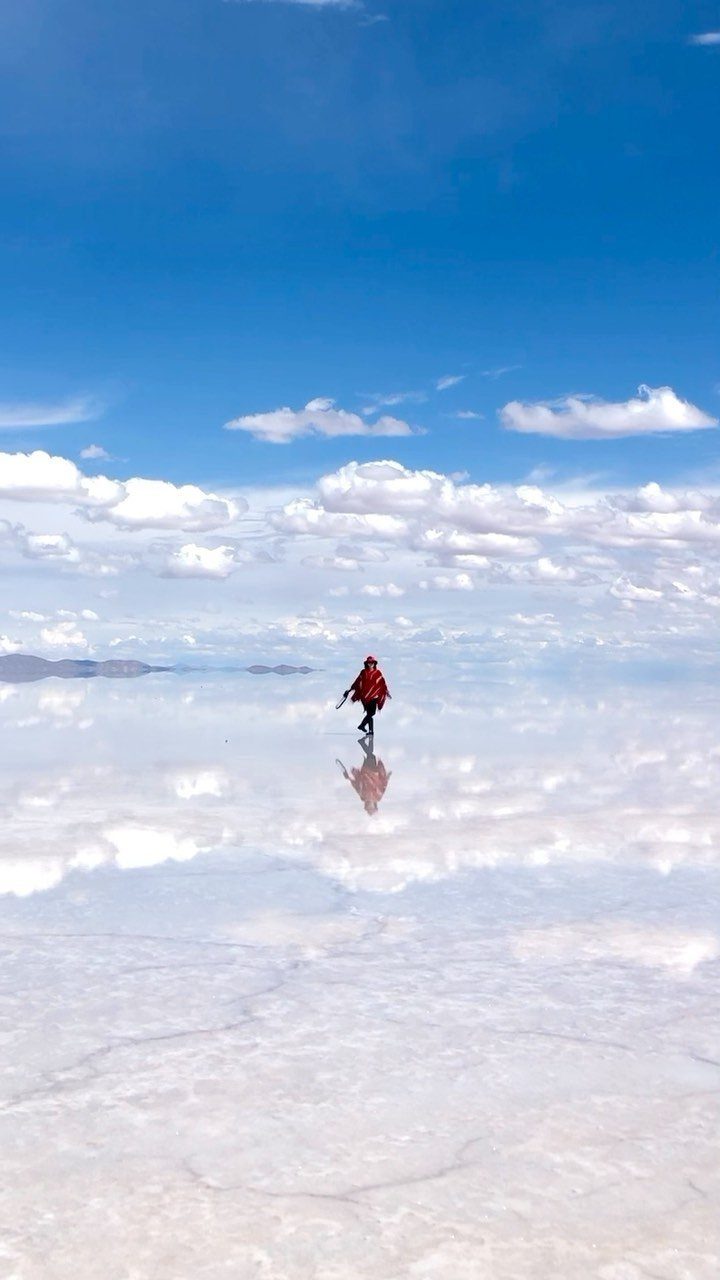 26 Pretty Places Around the World, From Fjords to Falls 6 Person in red walking on a reflective white salt flat under blue sky