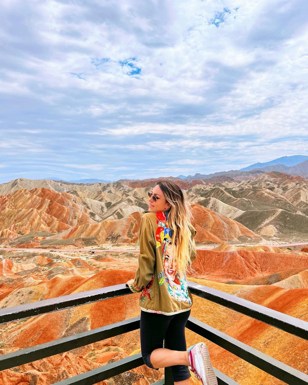 26 Pretty Places Around the World, From Fjords to Falls 20 Woman standing on a railing overlooking the colorful mountains of Zhangye National Geopark.