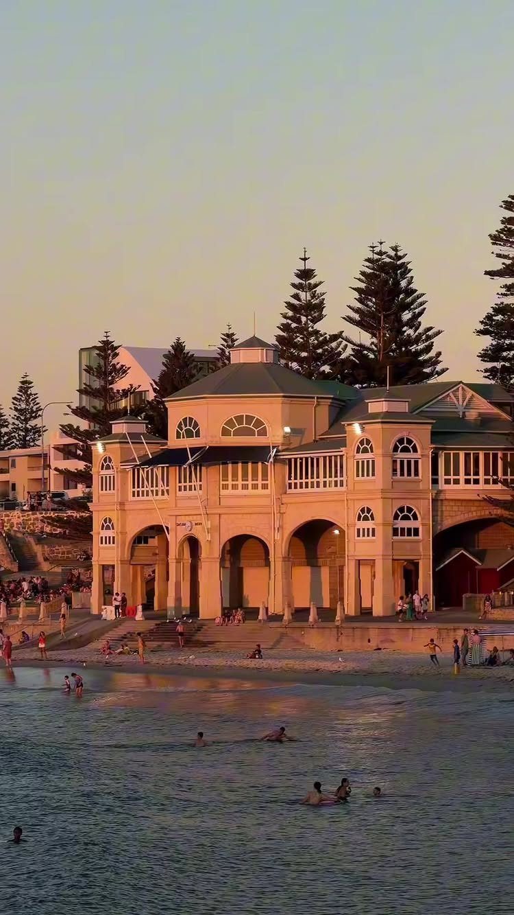 14 Pretty Places in Australia, from Reefs to Wine Regions 12 Cream pavilion building on a sandy beach with people swimming in the water.