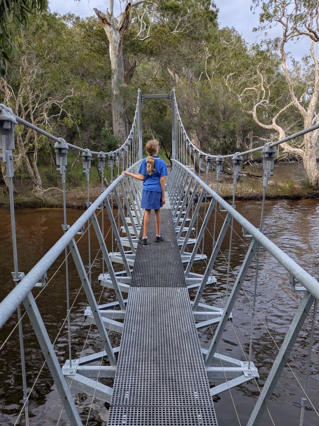 14 Pretty Places in Australia, from Reefs to Wine Regions 13 Girl standing on a metal suspension bridge over a river in a forest