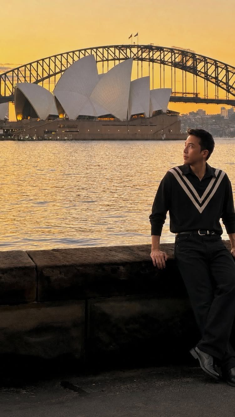 14 Pretty Places in Australia, from Reefs to Wine Regions 6 Man leaning on a stone wall with Sydney Opera House and Harbour Bridge behind.