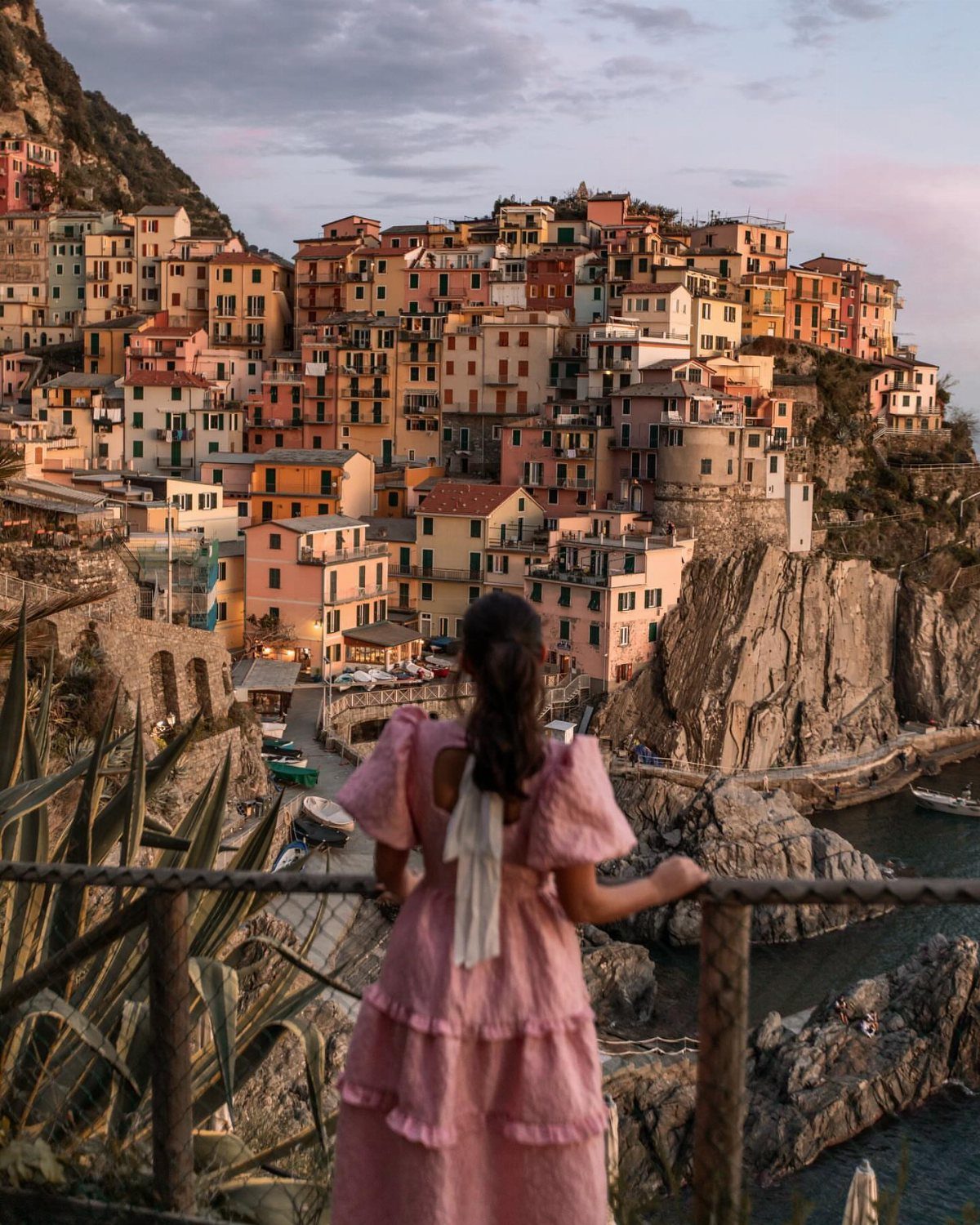 13 Pretty Places in Italy Worth Visiting in 2026 6 Woman in pink dress overlooking colorful cliffside houses in Cinque Terre, Italy.