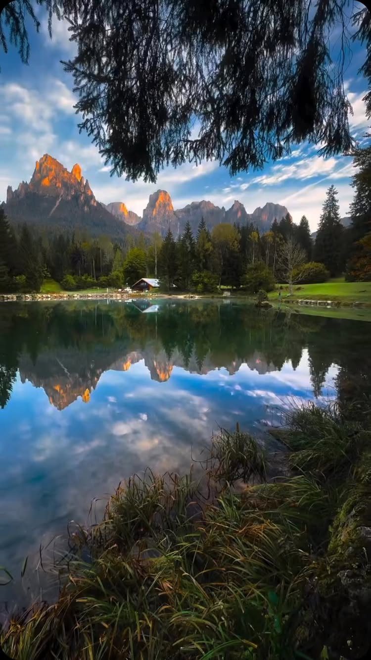13 Pretty Places in Italy Worth Visiting in 2026 8 Jagged mountain peaks reflected in a clear blue lake surrounded by green forests.