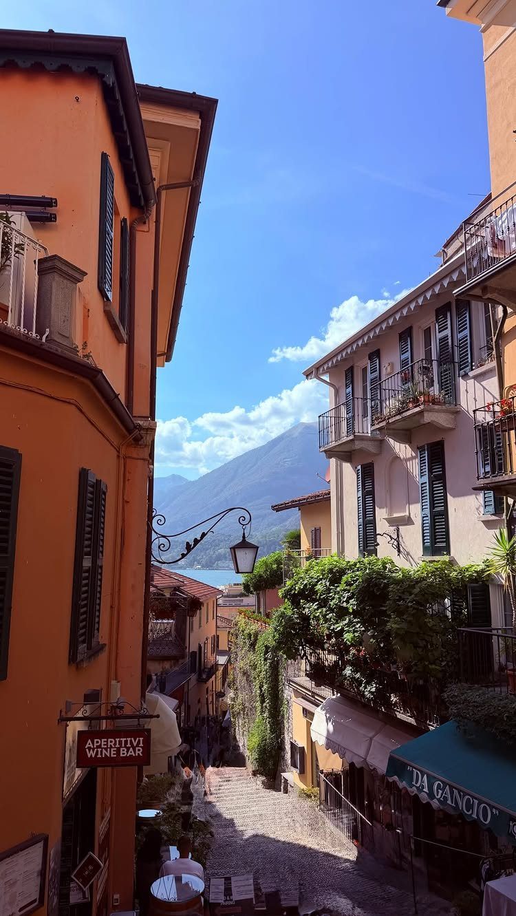 13 Pretty Places in Italy Worth Visiting in 2026 7 Narrow cobblestone street with colorful buildings leading toward a lake and distant mountains.
