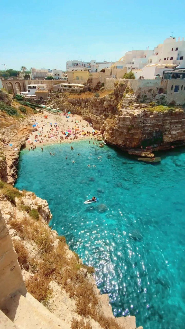 13 Pretty Places in Italy Worth Visiting in 2026 12 Turquoise cove beach surrounded by high limestone cliffs and white coastal buildings.