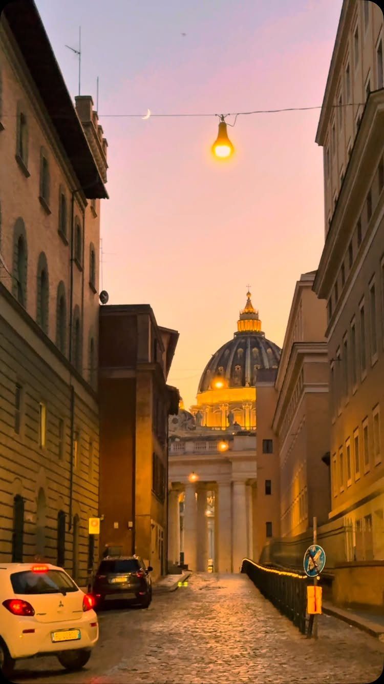 13 Pretty Places in Italy Worth Visiting in 2026 2 Cobblestone street leading toward the illuminated dome of St. Peter's Basilica at sunset.