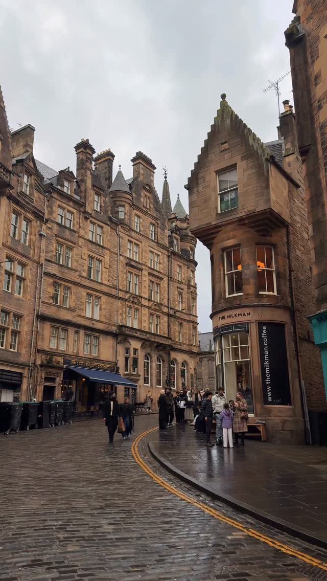 Historic brown stone buildings lining a wet cobblestone street in Edinburgh city center.