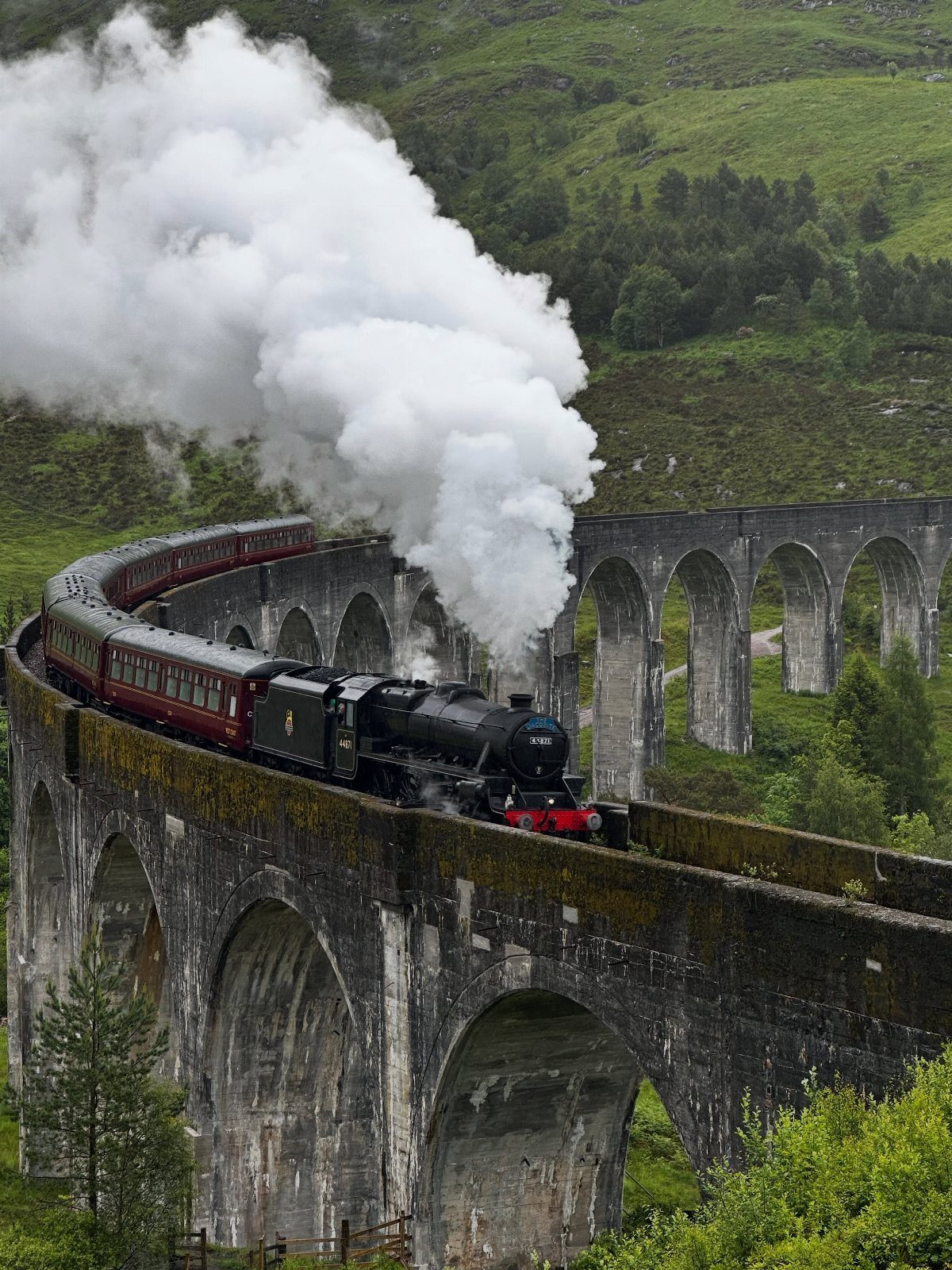 Steam train crossing a curved stone viaduct in the green Scottish Highlands