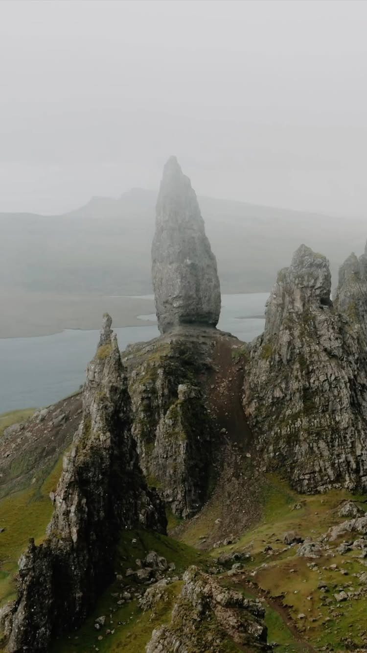 Jagged rock pinnacle on a green hillside overlooking a misty Scottish loch.