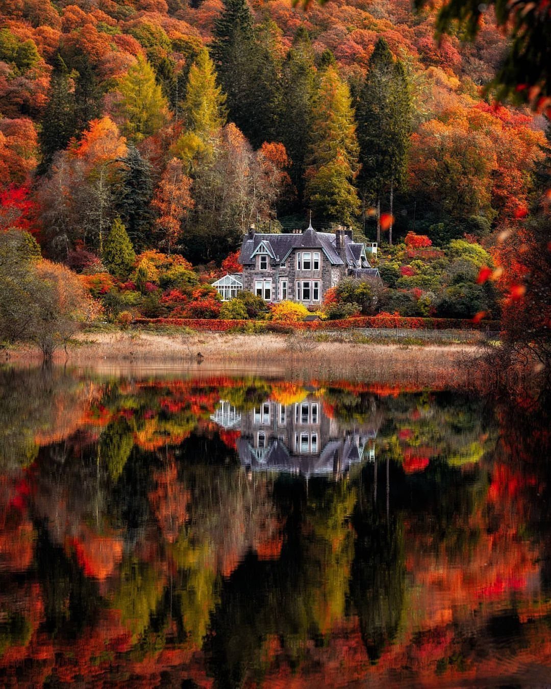 Stone house by a lake reflecting colorful autumn trees in a Scottish landscape
