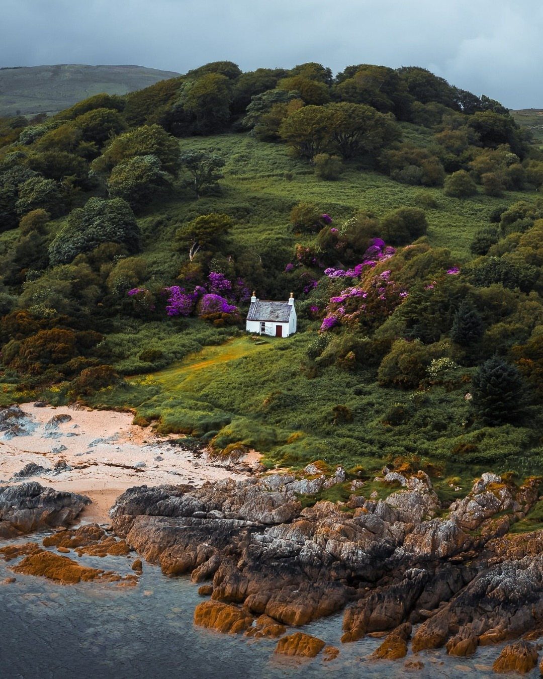 Small white cottage on a green hillside overlooking a rocky Scottish coastline