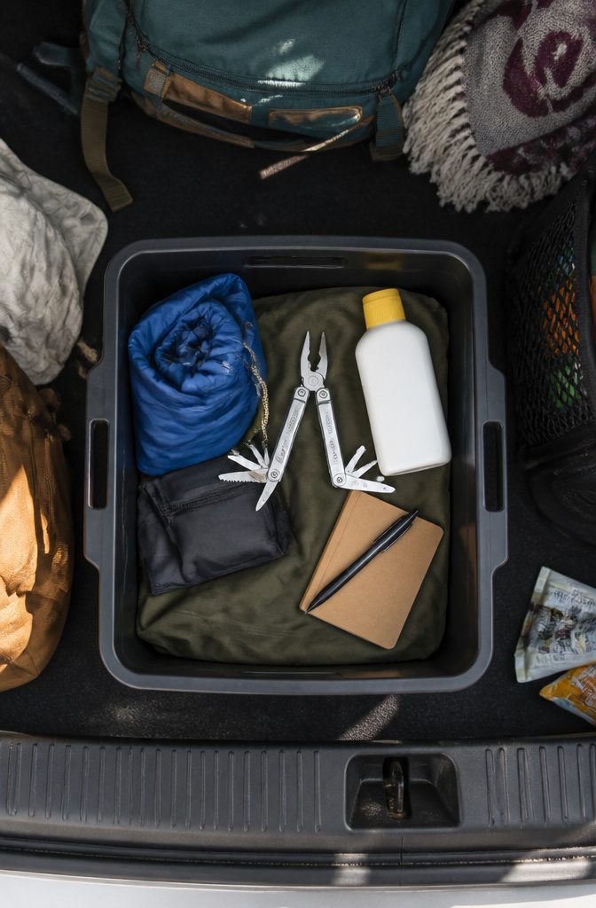 A bin in a car trunk containing sunscreen, a multi-tool, and more.