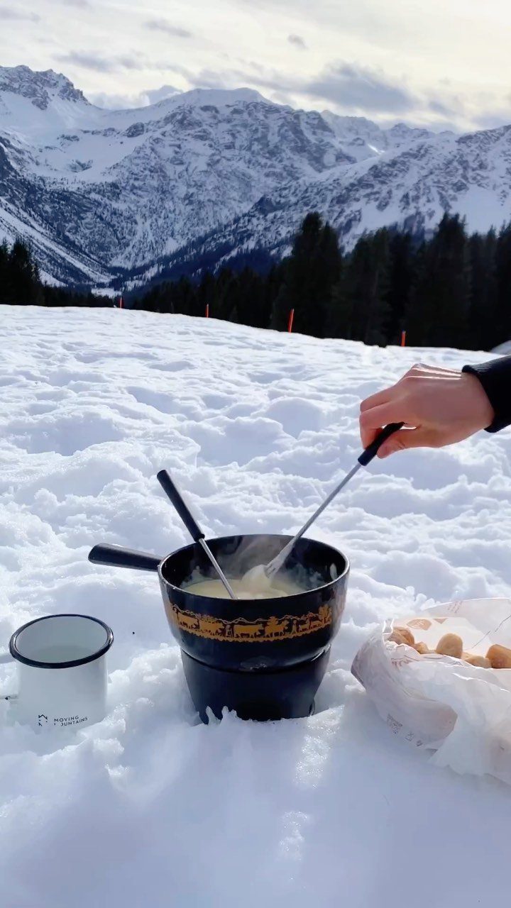 Cheese fondue pot in white snow with snow-capped mountains in the background