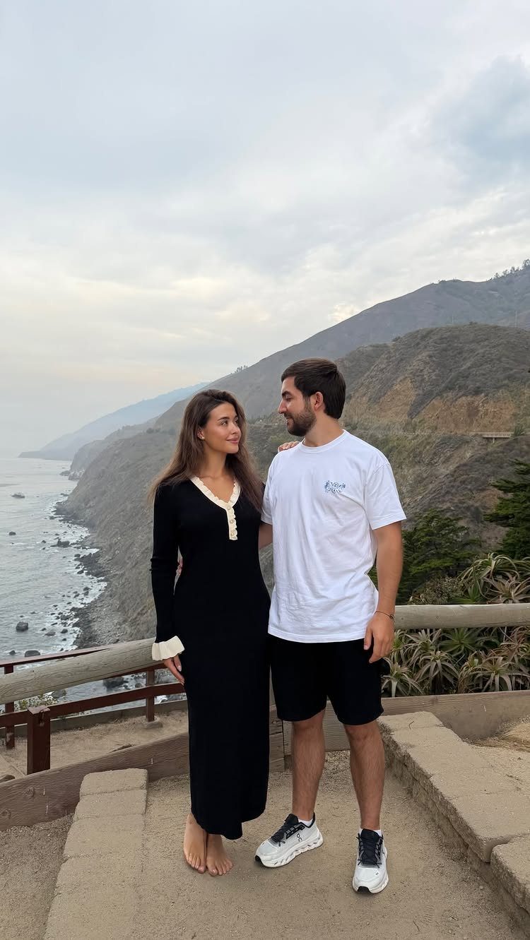 Couple standing on a cliffside path overlooking a dramatic rocky coastline and ocean.
