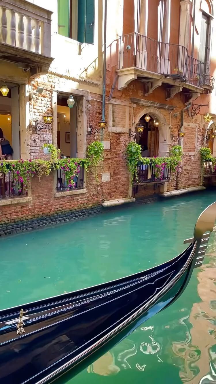 Black gondola bow on a turquoise Venetian canal lined with brick buildings.
