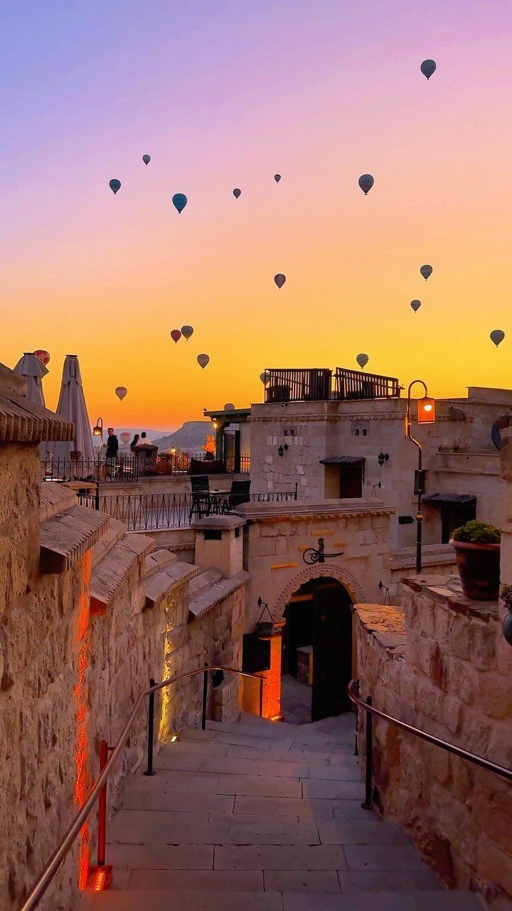 Hot air balloons floating over a stone village during a colorful sunrise sky.