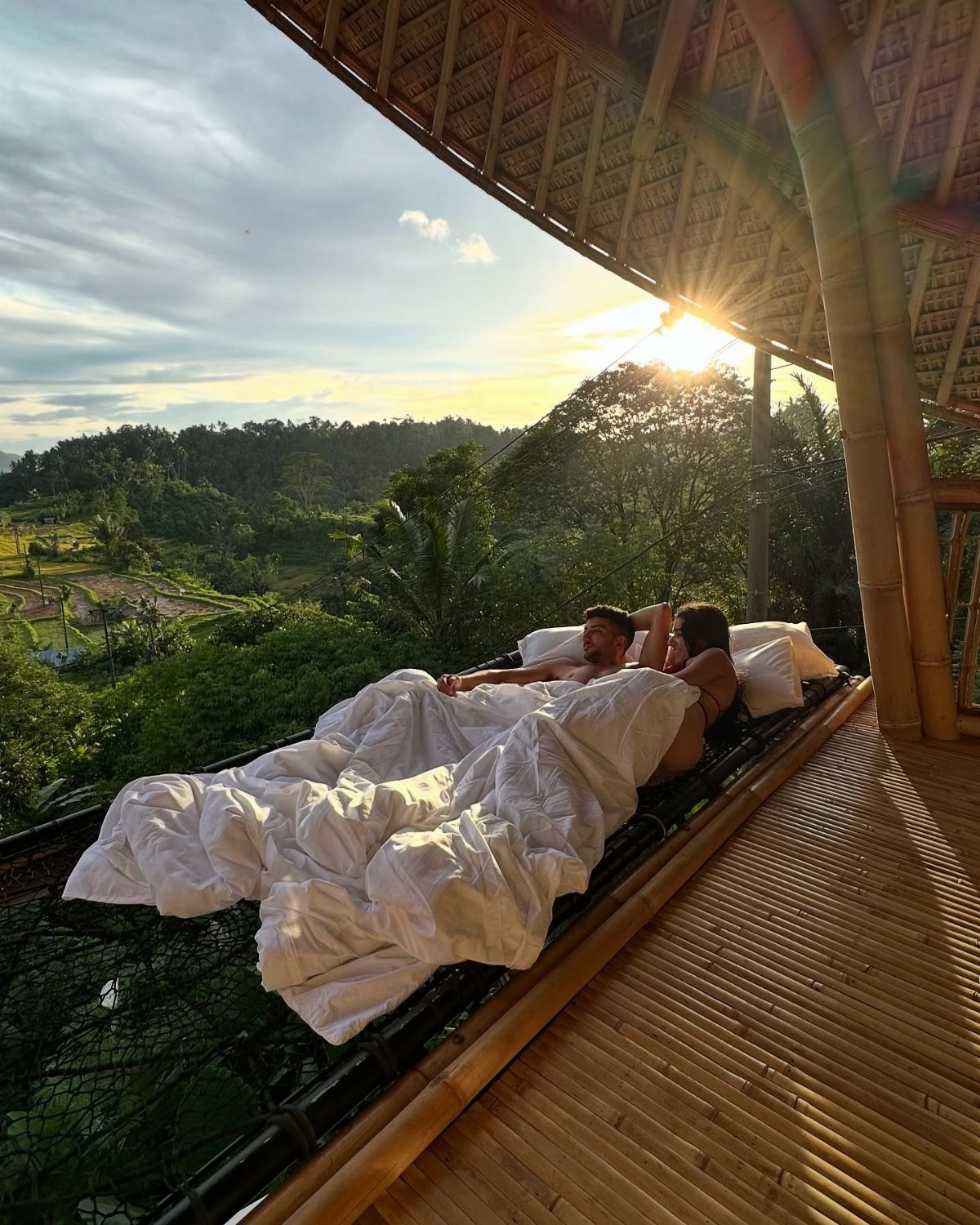 Couple relaxing in a bamboo bed overlooking a tropical valley at sunset