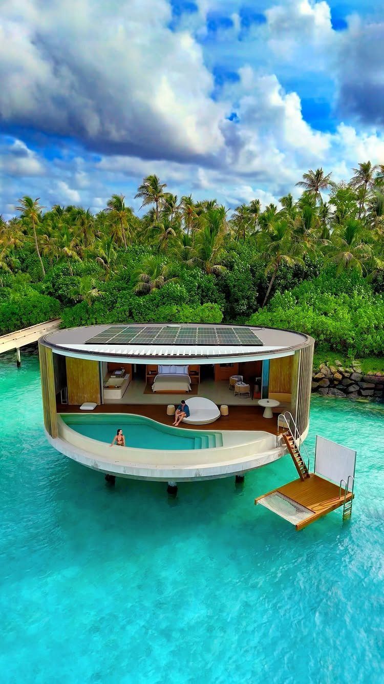 Circular overwater bungalow with a private pool in turquoise tropical waters and palm trees.