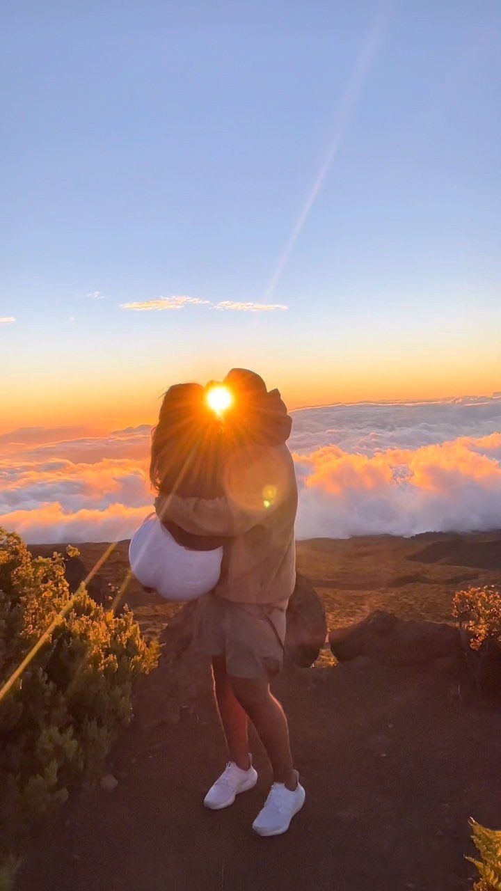 Couple kissing on a mountain peak above a sea of clouds at sunset.