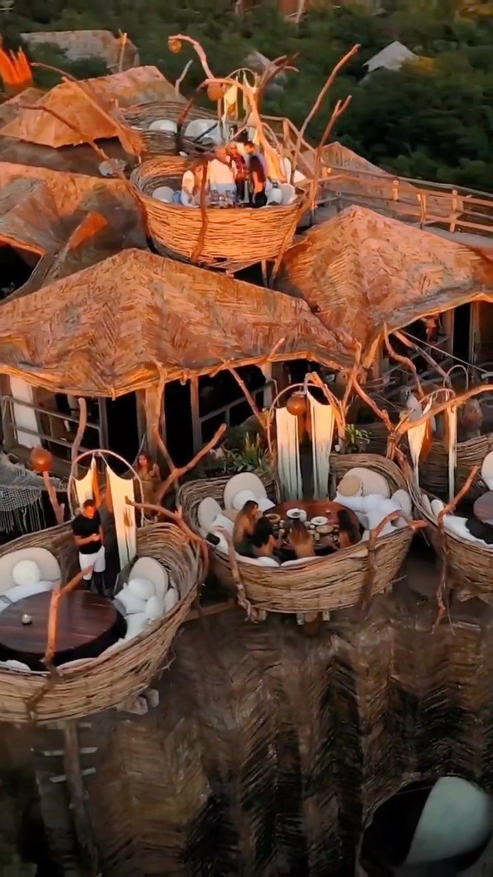 Woven wicker dining pods with thatched roofs overlooking a lush green landscape.