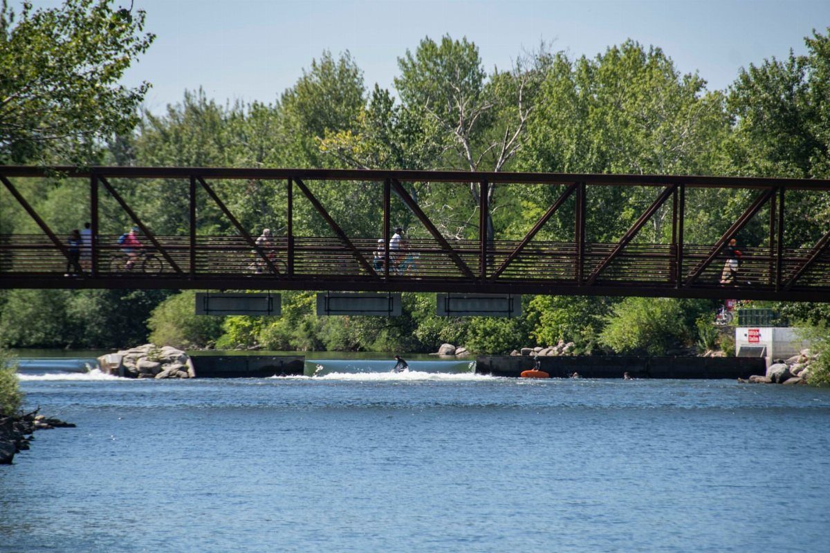 7 Sights to See in the US, From Acadia to Old Idaho 6 Brown metal truss bridge over a blue river with people walking and cycling.