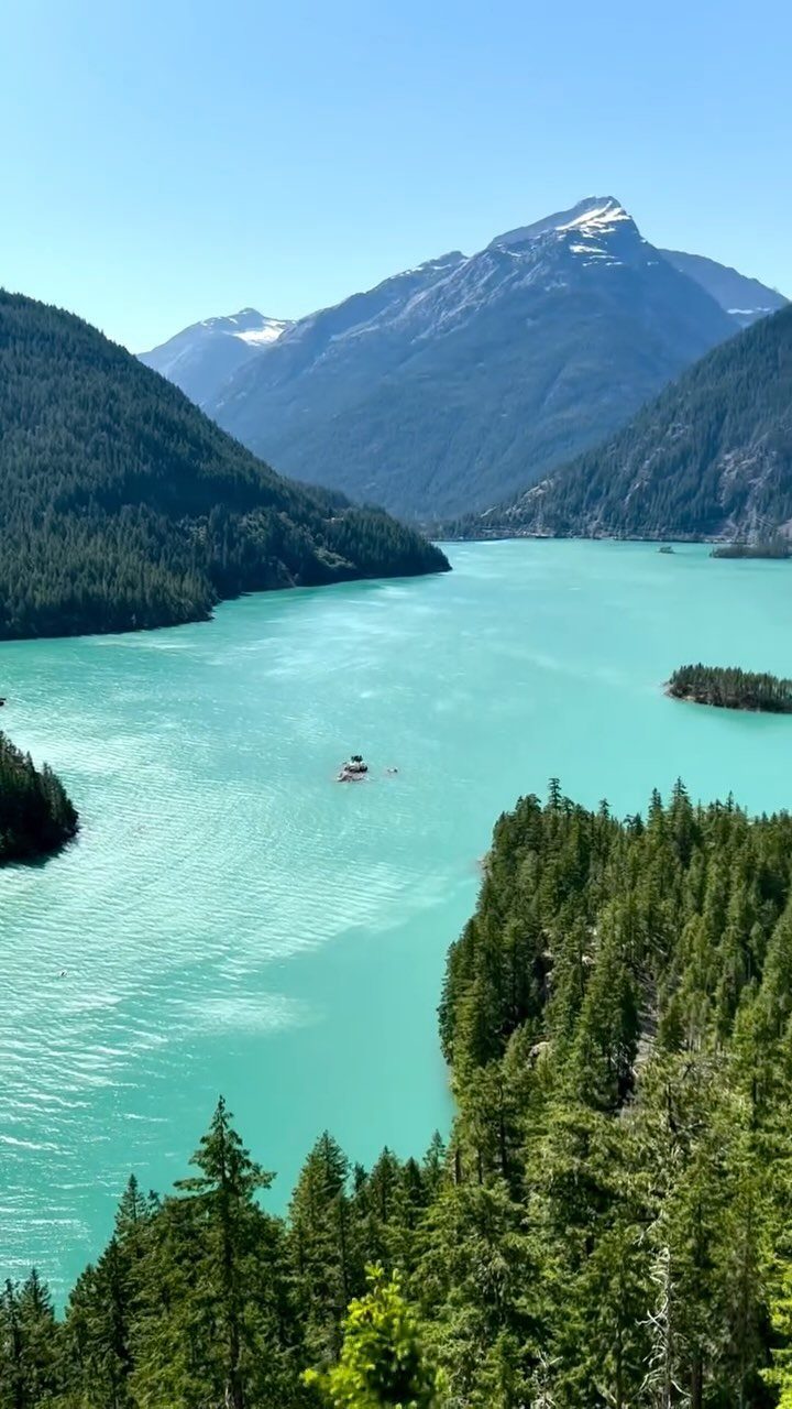 Turquoise glacial lake surrounded by steep forested mountains and evergreen trees.