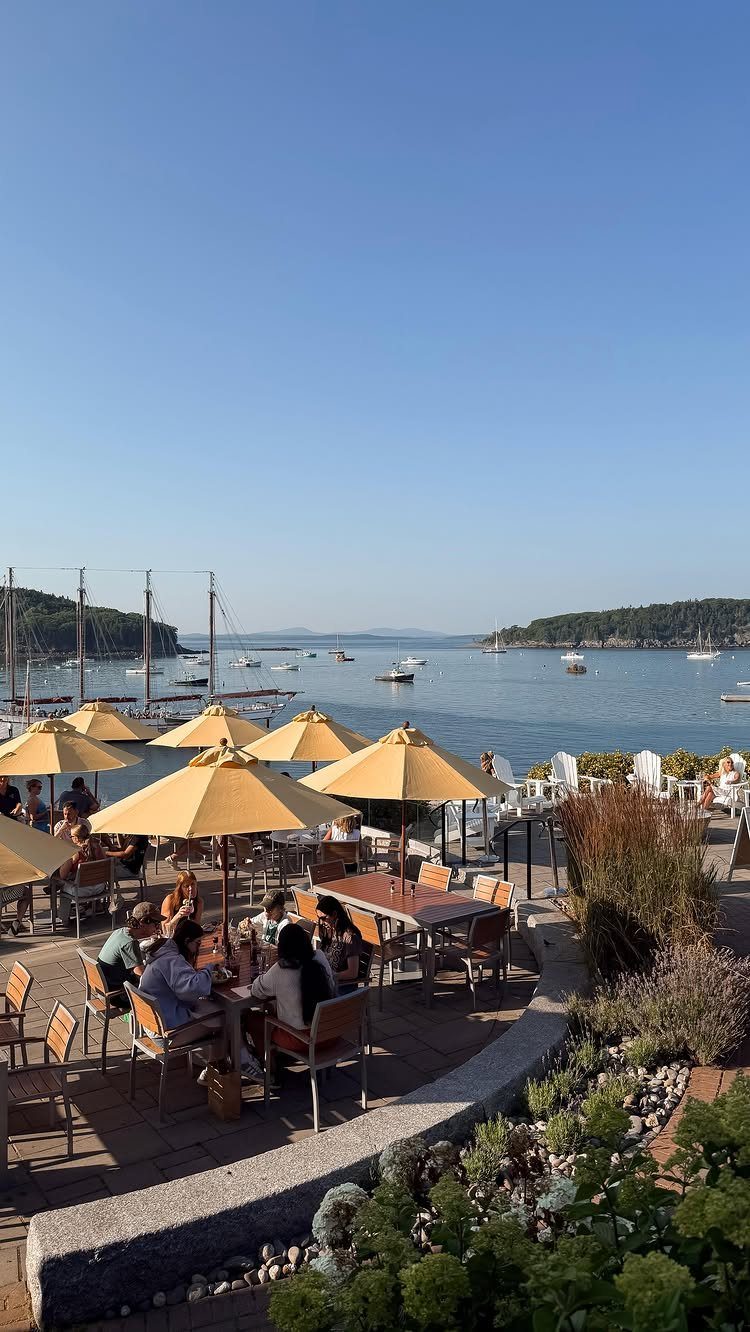 Outdoor patio with yellow umbrellas overlooking a blue bay with boats and hills.