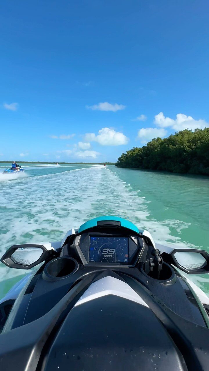 Jet ski dashboard on turquoise water with green mangroves under a blue sky