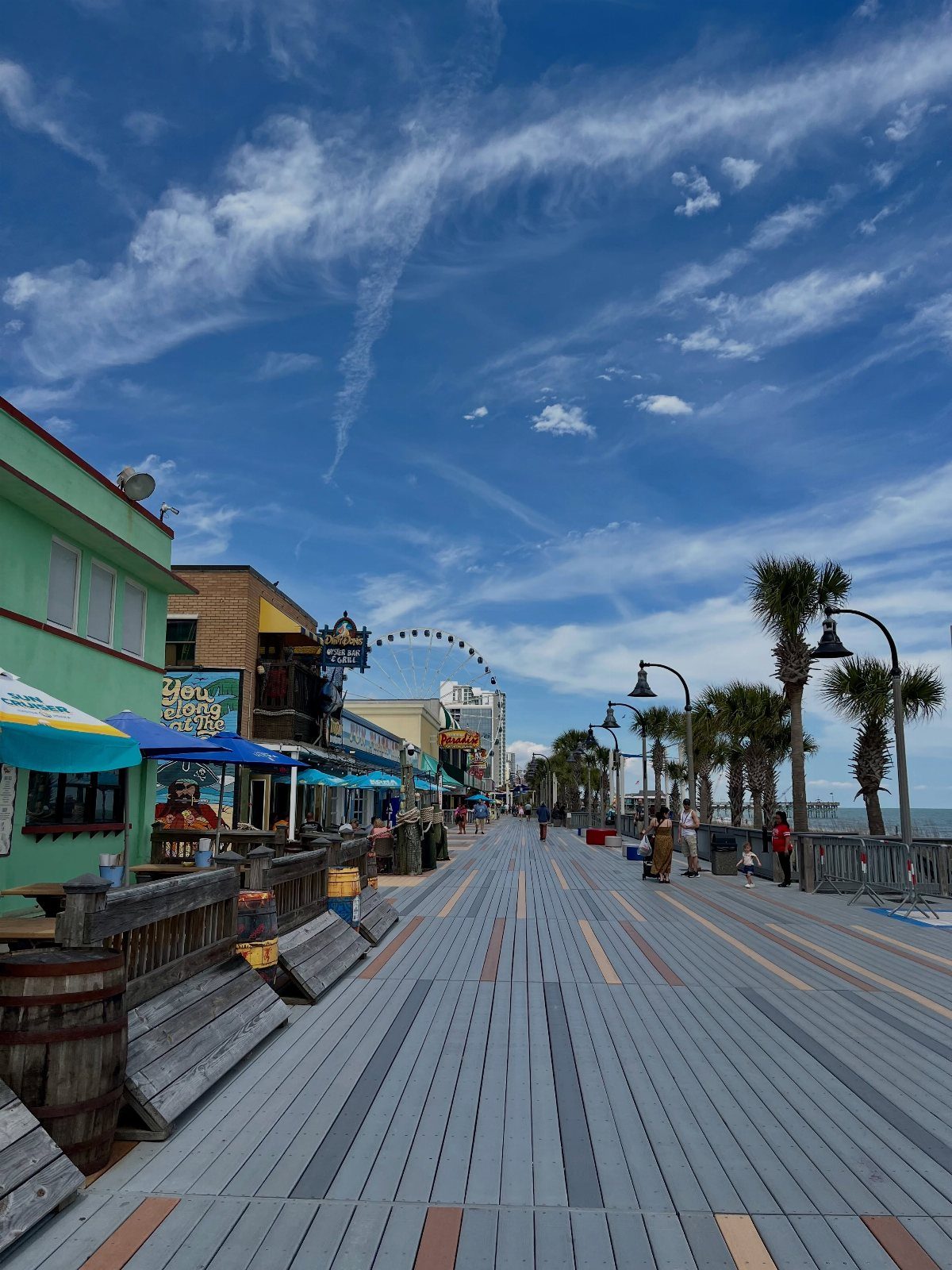 Wooden boardwalk with colorful shops and palm trees under a bright blue sky.