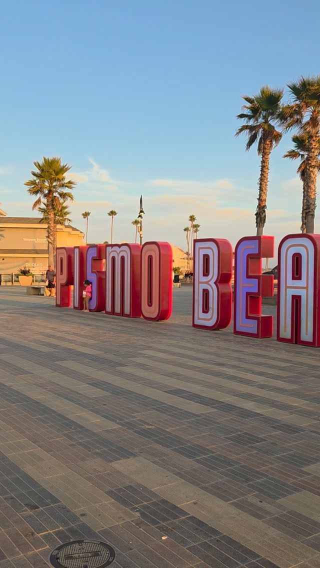 Pismo Beach sign in large colorful letters on a paved walkway with palm trees.