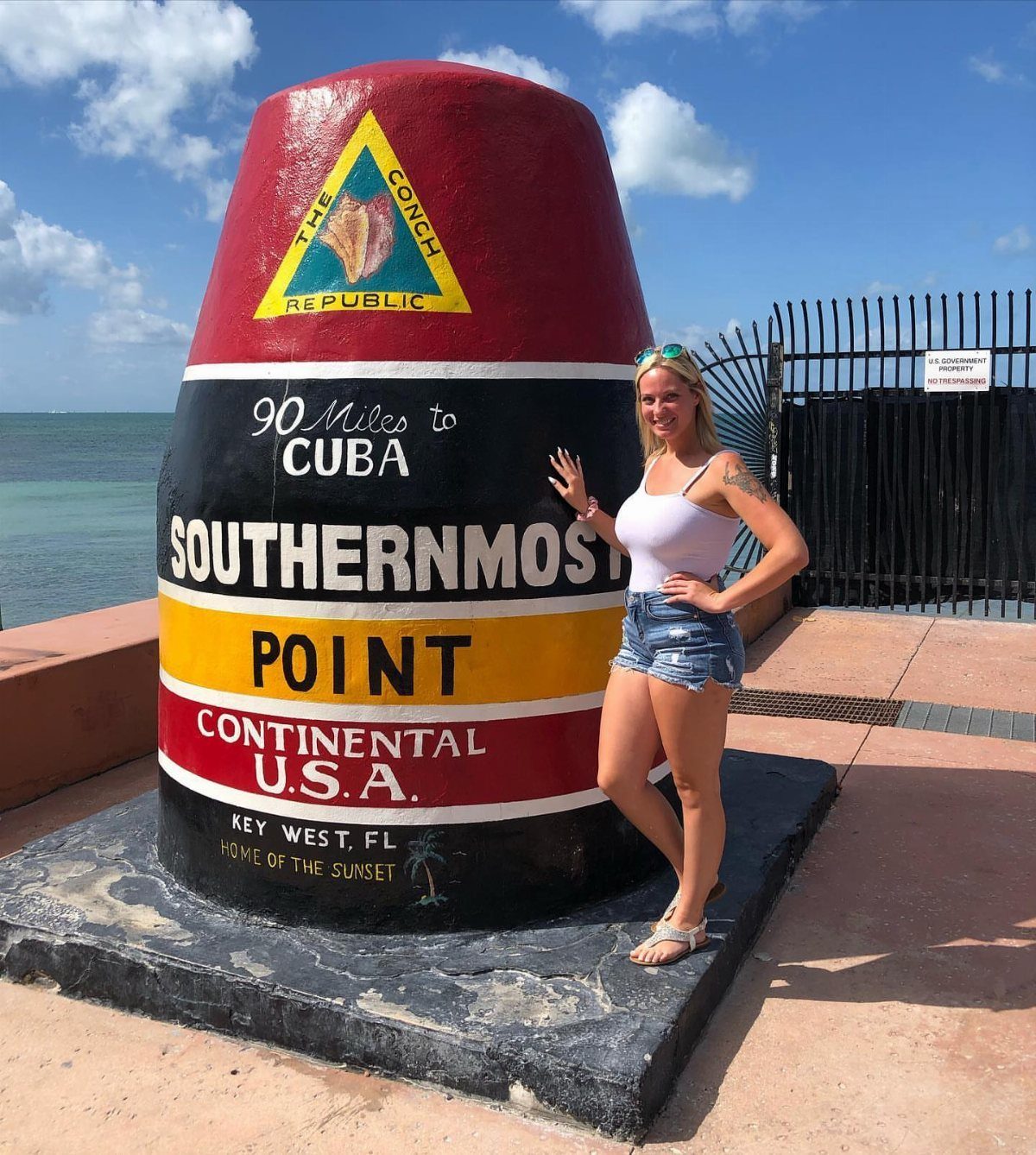 Woman posing by the Southernmost Point marker in Key West with ocean background