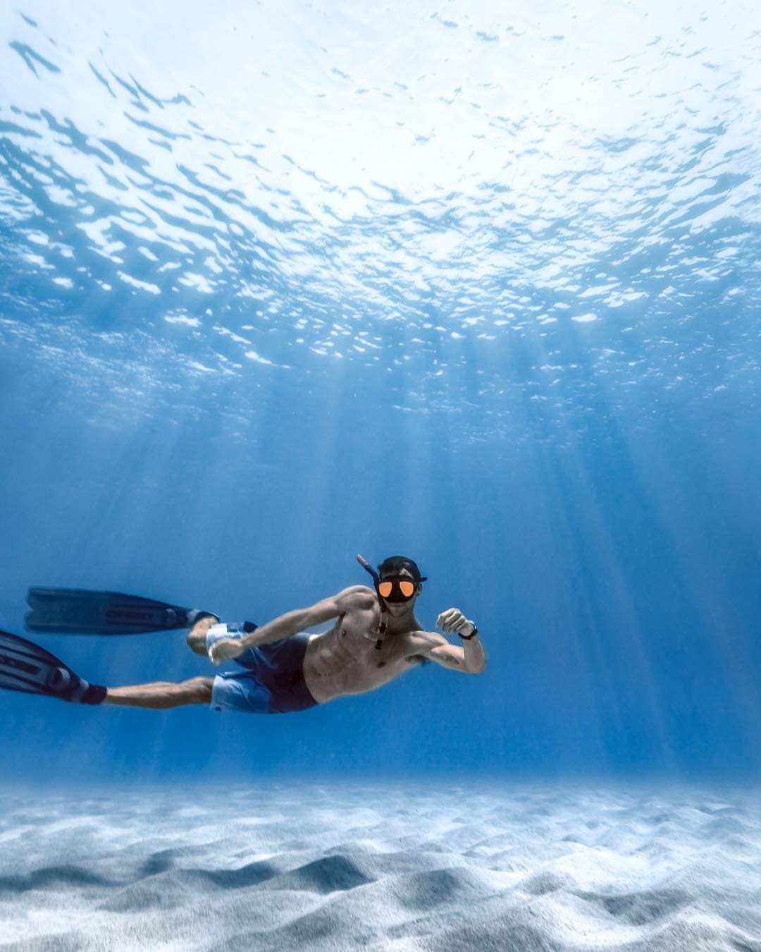 Man snorkeling in clear blue ocean water over a white sandy seabed